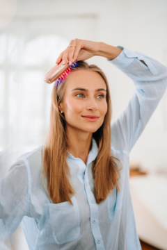 Kobieta używa złotego grzebienia Beautifly LaserBoost Pro z kolorowymi światłami LED do stymulacji porostu włosów.