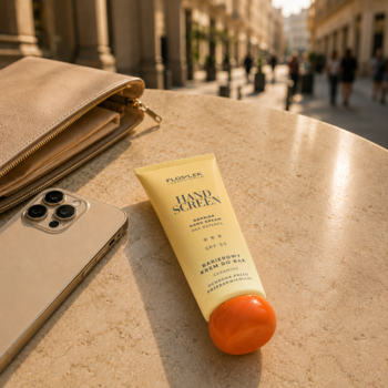 Żółty krem do rąk z filtrem SPF 50 na stole, obok beżowej kopertówki i smartfona, z miastem w tle.