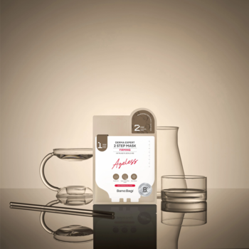 Dwuetapowa maska Banobagi Ageless w białej saszetce, obok szklane naczynia laboratoryjne na beżowym tle.