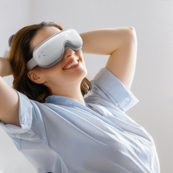 Uśmiechnięta kobieta w białym masażerze RENPHO Eyeris Smart na oczach, relaksuje się z rękami za głową.