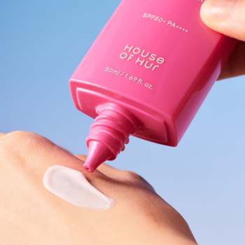 Różowy filtr przeciwsłoneczny HOUSE OF HUR SPF50+ PA++++ wyciskany na dłoń na tle błękitnego nieba.