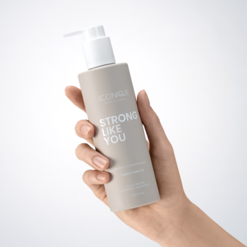 Dłoń trzyma beżowy spray termoochronny Iconique STRONG LIKE YOU z białą pompką, widoczny pod kątem.