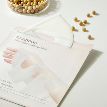 Maska w płachcie Mixsoon Bean Collagen Hydrogel częściowo wyjęta z opakowania, obok rozsypane ziarna soi na białym tle.
