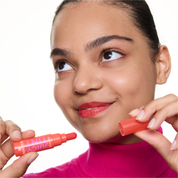 Kobieta trzyma otwarty, czerwony pisak do ust essence JUICY TINT 2 Strawberry Szn, patrząc w górę.