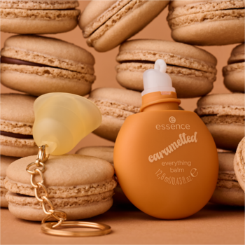 Pomarańczowy balsam essence caramelted z breloczkiem, na tle rozmytych, jasnobrązowych makaroników.