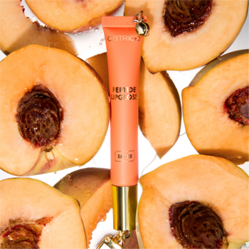 Catrice Peach Iced Tea błyszczyk SPF 25, brzoskwiniowa tubka z zawieszką, na błyszczącym tle pośród brzoskwiń.