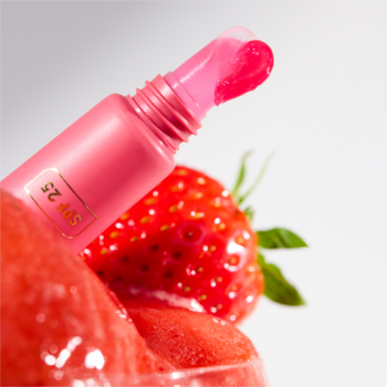 Zbliżenie: różowy błyszczyk Catrice Strawberry Sorbet SPF 25 wypływa z tubki, obok świeża truskawka i sorbet.