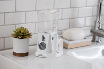 Biały irygator Waterpik WF-310 NANO na blacie łazienki, kompaktowy rozmiar z przezroczystym zbiornikiem.