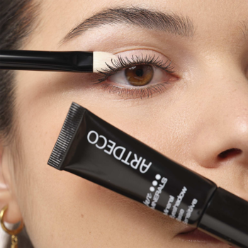 ARTDECO Mineral Eyeshadow Base w czarnej tubce. Kobieta aplikuje białą bazę pod cienie na powiekę pędzelkiem.