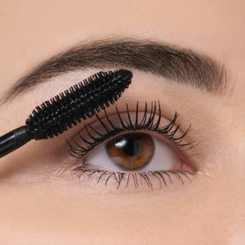 Zbliżenie na brązowe oko, aplikacja tuszu Volume Supreme Mascara czarną szczoteczką, rzęsy pogrubione i rozdzielone.