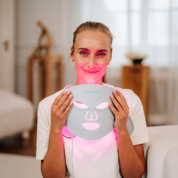 Beautifly AuraSkin Pro, maska LED do fototerapii, trzymana przez kobietę, emituje czerwone światło na twarz.