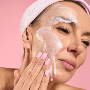 Kobieta w opasce nakłada pieniący się żel oczyszczający Swederm Glow Face Cleanser na twarz.