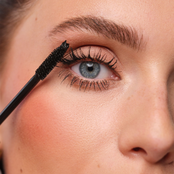Kobieta aplikuje czarny, wodoodporny tusz do rzęs ARTDECO All in One Mascara. Zbliżenie na oko z niebieską tęczówką.