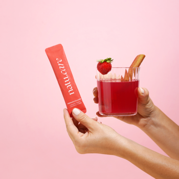 Ręce trzymają koralową saszetkę Natu.Care Premium Collagen i szklankę różowego napoju z truskawką i rabarbarem.