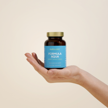 Ręka trzyma brązową butelkę suplementu Formula Aqua Natu.Care z niebieską etykietą, wspiera lekkość.