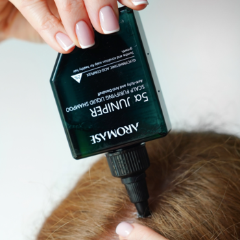 Aromase 5α Juniper peeling do skóry głowy, aplikowany dłonią na brązowe włosy, zbliżenie.