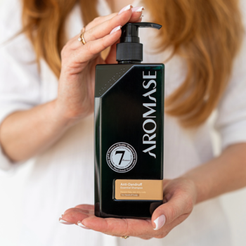 Szampon przeciwłupieżowy Aromase w czarnej butelce z pompką, pionowo w dłoniach, widoczne logo '7'.