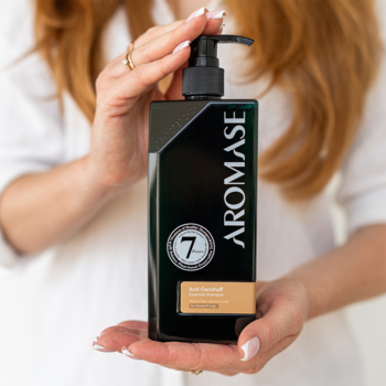 AROMASE Anti-Dandruff Shampoo, czarna butelka z pompką, etykieta z "7", trzymany w dłoniach na białej koszuli.