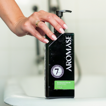 Czarny szampon seboregulujący AROMASE 5α Anti-oil w butelce z pompką, trzymany w dłoni nad wanną.