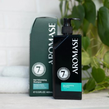 Aromase Hair Volumizing Shampoo: czarna butelka z pompką i zielony kartonik, logo '7', na jasnym blacie z rośliną.