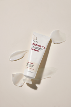 Nacific Rice+Pepta Collagen Sherbet Cleansing Balm, biała tubka ukośnie na jasnym tle, otoczona rozmazanym produktem.