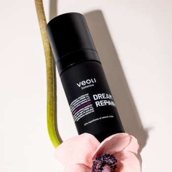 Czarna butelka Veoli DREAM REPAIR regenerujący krem na noc, z pompką, na tle zielonego pędu i różowego kwiatu.