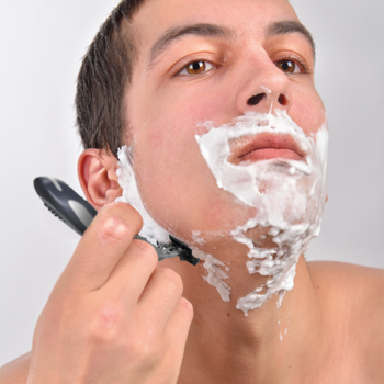 Mężczyzna goli policzek, używając męskiej maszynki do golenia, twarz pokryta białą pianką. Zbliżenie.