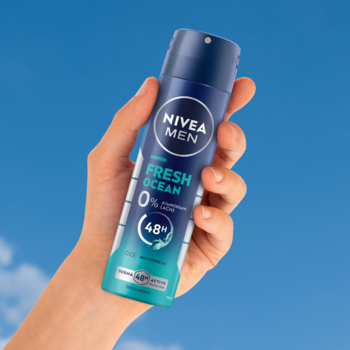 Niebiesko-turkusowy dezodorant NIVEA MEN Fresh Ocean w sprayu, 0% aluminium, trzymany w dłoni na tle błękitnego nieba.
