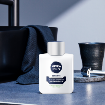 NIVEA MEN SENSITIVE Łagodzący Balsam po goleniu, biała butelka na blacie w łazience z czarną umywalką.