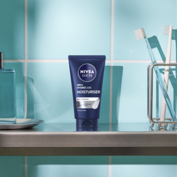 Krem nawilżający NIVEA MEN Protect & Care 24h w ciemnoniebieskiej tubce, stoi na łazienkowej półce.
