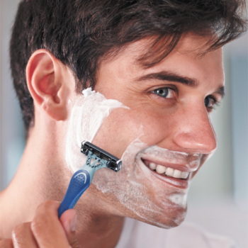 Uśmiechnięty mężczyzna goli twarz maszynką BIC Flex 3 z niebieską rączką i 3 ostrzami, widoczna biała piana.