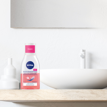 NIVEA Dwufazowy płyn do demakijażu oczu, różowo-przezroczysta butelka z Witaminą C na drewnianej półce w łazience.