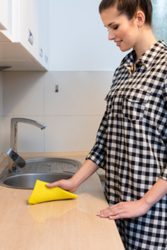 Kobieta czyści blat żółtą, chłonną pucerką kuchenną. Produkt higieniczny i trwały, widok z boku w akcji.