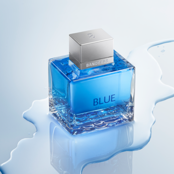 Blue Seduction Banderas, świeża męska woda toaletowa w niebieskiej butelce z mozaiką, na tle rozlanej wody.