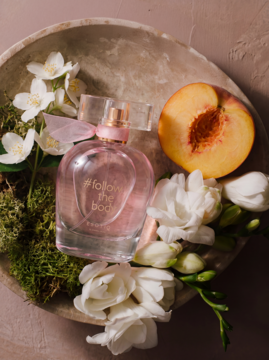 Damska woda perfumowana Esotiq #follow the body, różowa butelka z brzoskwinią, białymi kwiatami i mchem w kamiennej misie.