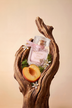 Damska woda perfumowana Esotiq #follow the body, butelka z różową etykietą, w gnarled drewnie obok brzoskwini.