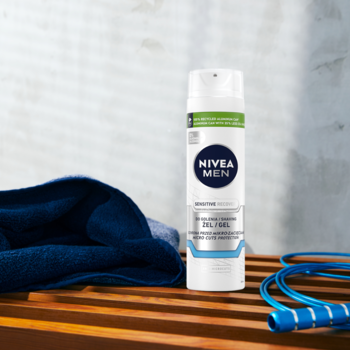 Biała butelka NIVEA MEN Sensitive Żel do golenia na drewnianej ławce obok niebieskiego ręcznika i skakanki.