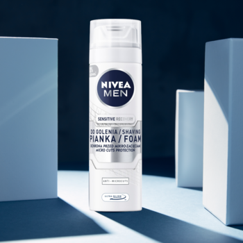 Biała butelka NIVEA MEN Sensitive pianka do golenia, widok z przodu, na niebieskim tle z blokami.