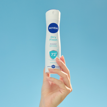 NIVEA Dry Fresh antyperspirant w białym sprayu, trzymany w dłoni na tle błękitnego nieba, 72h ochrony.