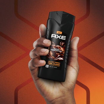 Czarna butelka żelu AXE Dark Temptation 3w1 z pomarańczową etykietą, trzymana w dłoni na tle wzoru.