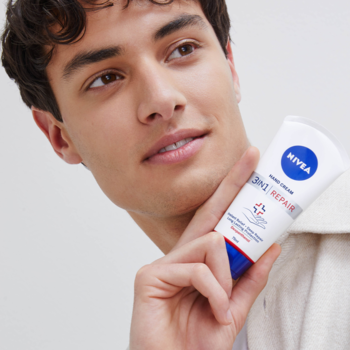 Mężczyzna uśmiecha się, trzymając białą tubkę kremu do rąk NIVEA Repair Care z niebieskimi i czerwonymi detalami.