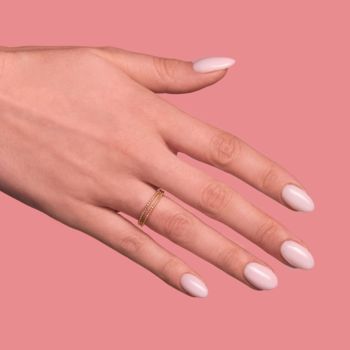 Lakier hybrydowy Semilac 032 Biscuit. Dłoń z jasnoróżowymi paznokciami i złotym pierścionkiem na koralowym tle.