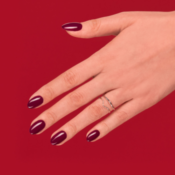 Dłoń z długimi paznokciami w kolorze Semilac 083 Burgundy Wine (głęboki fiolet), na czerwonym tle.