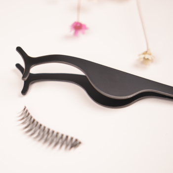 Czarne, wyprofilowane szczypce do sztucznych rzęs i rzęsy na pasku na jasnym, rozmazanym tle.