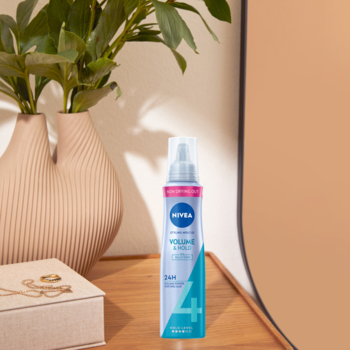 Pianka do włosów NIVEA Volume & Hold, lawendowa butelka 150ml z białym dozownikiem, na drewnianym blacie.