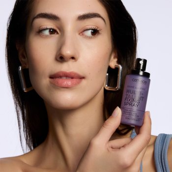 Kobieta trzyma fioletowy Catrice Multi-Talent Fixing Spray, wielofunkcyjny spray utrwalający makijaż, zbliżenie.
