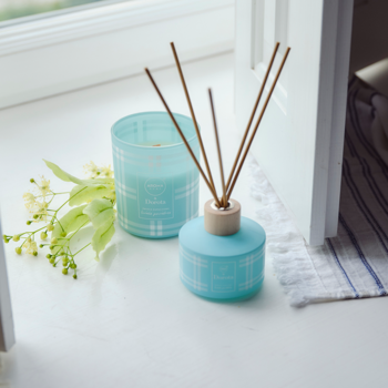 Aroma Home & Dorota: turkusowa świeca i dyfuzor z patyczkami, biały wzór, na parapecie z zielonymi kwiatami.