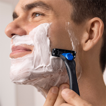Bliskie ujęcie mężczyzny goli twarz białą pianką, używając czarno-niebieskiej golarki BIC Hybrid 3 Flex.