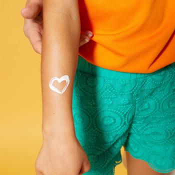 Dziecięca ręka z narysowanym sercem z białego NIVEA SUN KIDS Balsam ochronny SPF 50+ na ramieniu, tło żółte.