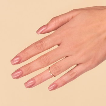 Dłoń z hybrydowym lakierem do paznokci w jasnym karmelu z brokatowym pyłkiem, delikatny złoty pierścionek.